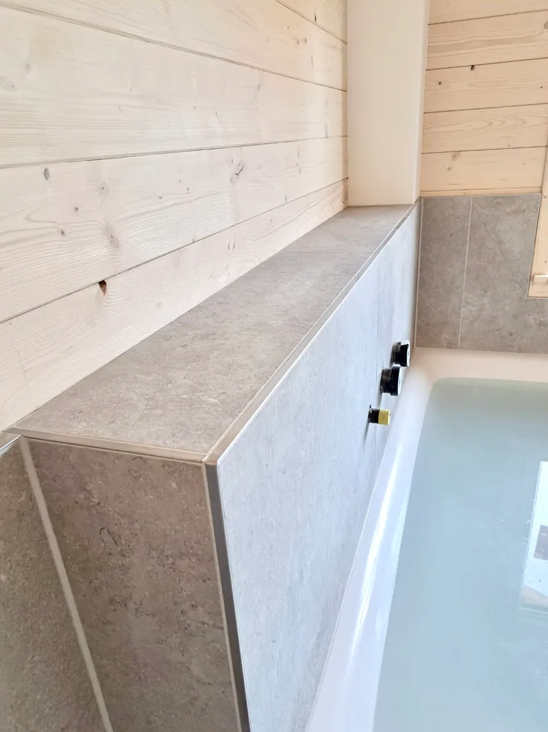 Badewanne mit gefliester Verkleidung neben Holzwand