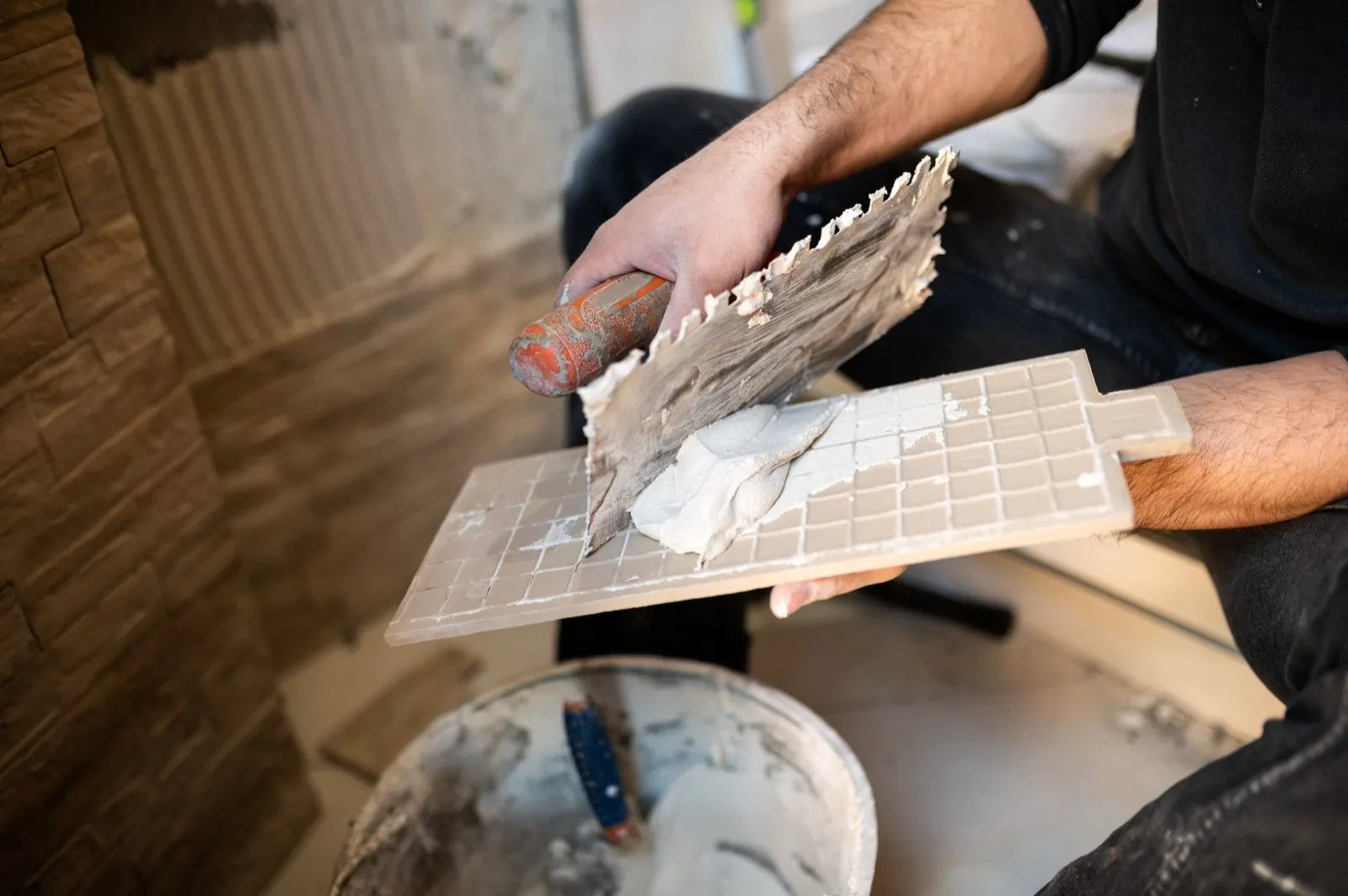 Fliesenleger trägt mit der Zahnkelle Fliesenkleber auf eine Fliese auf